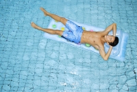 Man lying on pool raft, hands behind head - Asia Images Group