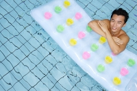 Man in swimming pool, leaning arms on pool raft - Asia Images Group