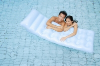 Couple in swimming pool leaning on pool raft - Asia Images Group