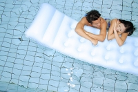 Couple in swimming pool leaning on pool raft, side by side - Asia Images Group