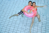 Couple in swimming pool holding on to inflatable ring - Asia Images Group