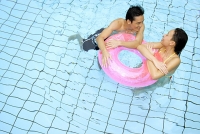 Couple in swimming pool leaning on inflatable ring - Asia Images Group