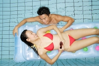 Woman lying on pool raft, man in water next to her - Asia Images Group