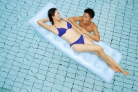 Woman lying on pool raft, smiling at man in water next to her - Asia Images Group
