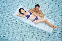 Woman in blue bikini lying on pool raft, man in water next to her - Asia Images Group