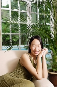 Woman on arm chair, smiling at camera, hands clasped - Asia Images Group