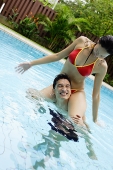 Couple in swimming pool, woman sitting on mans shoulders - Asia Images Group