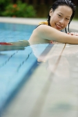 Woman leaning on the edge of swimming pool, smiling - Asia Images Group