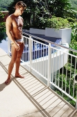 Man in swimming trunks, standing, looking down - Asia Images Group