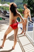 Couple in swimwear, woman standing in front of man, hand on hip, hand on head - Asia Images Group
