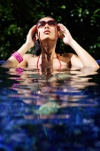 Woman sitting in swimming pool, touching sunglasses - Asia Images Group