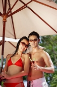 Couple standing under umbrella, holding drinks - Asia Images Group