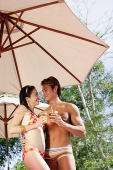 Couple standing under umbrella, holding drinks, looking at each other - Asia Images Group