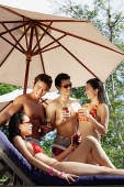 Young adults standing and holding drinks, one woman sitting on deck chair - Asia Images Group