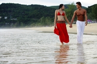 Couple walking side by side along beach, holding hands, looking at each other - Asia Images Group