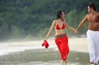 Couple running along beach, ankle deep in water, holding hands - Asia Images Group