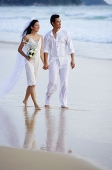 Bride and groom walking on beach, holding hands - Asia Images Group