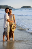 Couple standing on beach, ankle deep in water, looking at camera - Asia Images Group