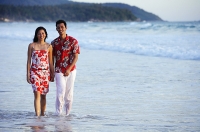 Couple walking on beach, ankle deep in water, holding hands, smiling at camera - Asia Images Group