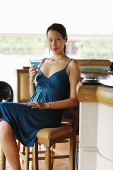Woman sitting at bar counter, holding drink, looking at camera - Asia Images Group