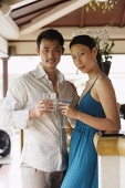 Couple standing side by side, holding drinks, looking at camera - Asia Images Group