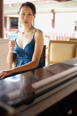 Woman sitting at bar counter, holding cocktail, looking at camera - Asia Images Group