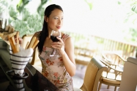 Woman sitting at bar counter, drinking wine, looking away - Asia Images Group