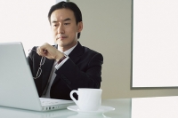Businessman sitting at table, looking at laptop - Asia Images Group
