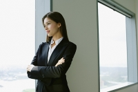 Businesswoman standing next to window in conference room, arms crossed - Asia Images Group