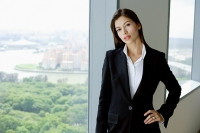 Businesswoman standing next to window in conference room, hand on hip, looking at camera - Asia Images Group
