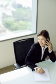 Businesswoman sitting at table, using mobile phone, looking away - Asia Images Group