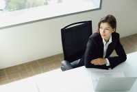 Businesswoman sitting at table, arms crossed, laptop in front of her - Asia Images Group