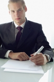 Businessman sitting at table with pen and paper, looking at camera - Asia Images Group