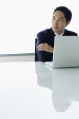 Businessman with laptop open in front of him, looking away - Asia Images Group