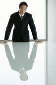 Businessman standing with hands on table, looking at camera - Asia Images Group