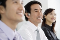 Executives in a row, wearing headsets, looking away, smiling - Asia Images Group
