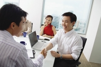 Two businessmen exchanging business cards, woman looking at them - Asia Images Group