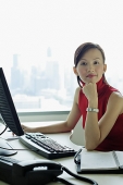 Female executive sitting at office desk, looking at camera - Asia Images Group