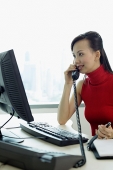 Female executive sitting at office desk, using telephone - Asia Images Group