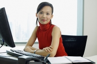 Female executive sitting at office desk, portrait - Asia Images Group