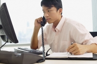 Male executive sitting at office desk, using telephone - Asia Images Group