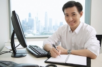 Male executive sitting at office desk, looking at camera, smiling - Asia Images Group