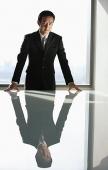 Businessman leaning on table, looking at camera - Asia Images Group