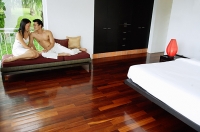 Couple in bedroom, sitting on daybed, looking at each other - Asia Images Group