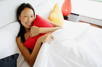 Woman lying in bed, hugging pillow, looking at camera - Asia Images Group