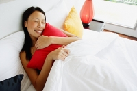 Woman lying in bed, hugging pillow, eyes closed - Asia Images Group