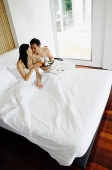 Couple having breakfast in bed, woman smiling at camera, high angle view - Asia Images Group