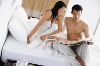 Couple sitting on bed, looking at newspaper - Asia Images Group