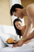 Woman in bed, man bringing breakfast tray - Asia Images Group