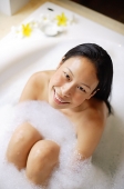 Woman sitting in bathtub, smiling up at camera - Asia Images Group